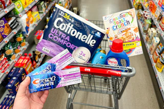 person holding crest toothpaste in front of a cart with cottonelle toilet paper, ogx shampoo, persil detergent, and cereal