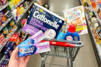 person holding crest toothpaste in front of a cart with cottonelle toilet paper, ogx shampoo, persil detergent, and cereal