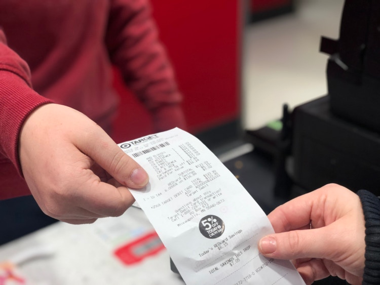 A customer's hand giving a Target receipt to a Target employee at the return counter.