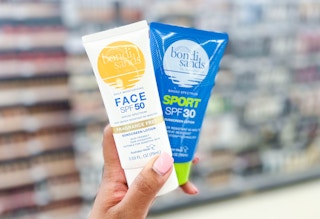 Hand holding bottle of Bondi Sands Face SPF50 lotion and Bondi Sands Sport SPF30 lotion in aisle