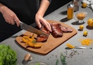 a person chopping meat on a bamboo cutting board