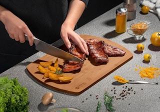 a person chopping meat on a bamboo cutting board