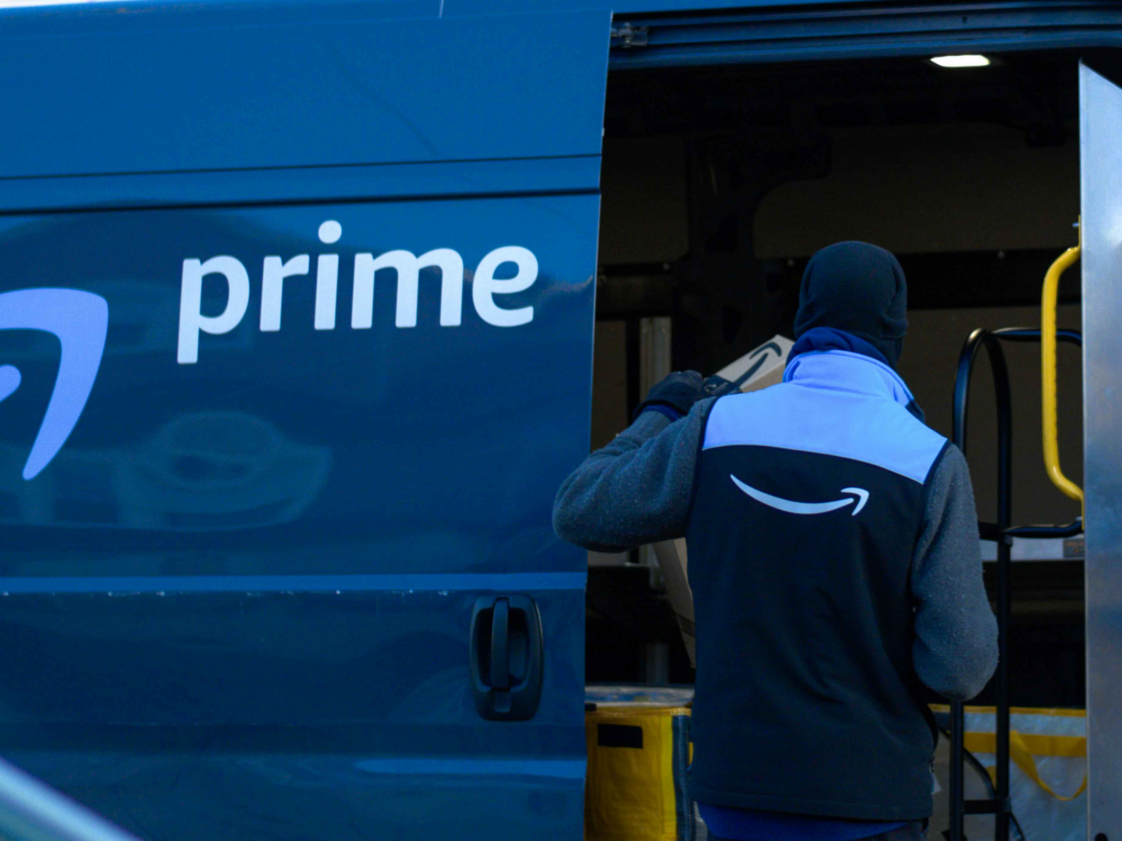 An Amazon delivery van driver opening the side door of the van to grab a package.