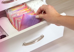 a hand pulling out a wrapped panty liner out of a drawer