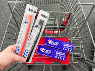 hand holding two oral b brilliance toothbrushes and two Crest toothpaste in the cart