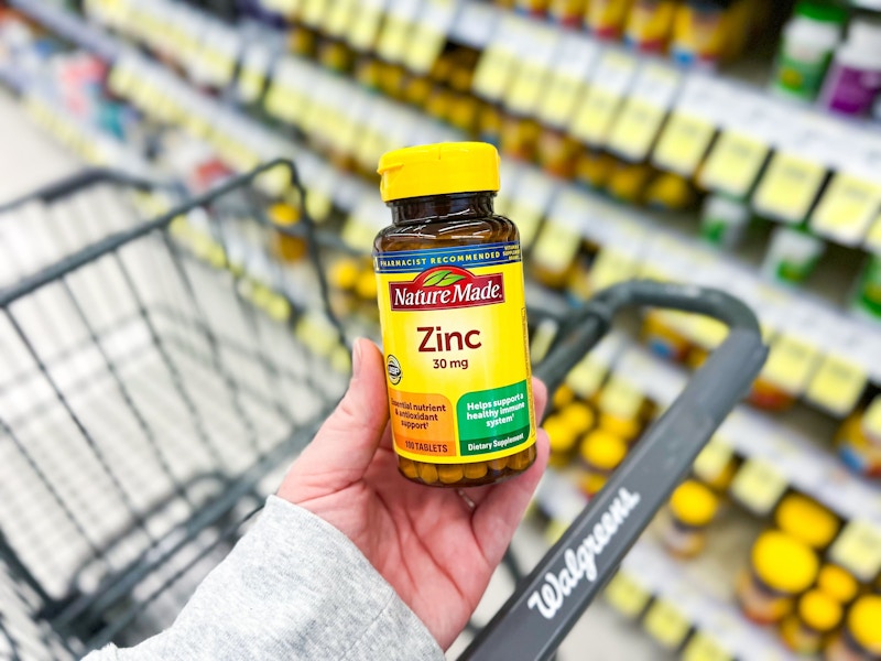 person holding a bottle of zinc tablets over a walgreens cart