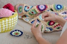 A person's hands as they work on crocheting a square for a blanket.