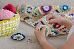 A person's hands as they work on crocheting a square for a blanket.