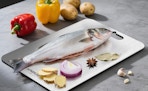 a fish and seasonings on a cutting board next to peppers and potatoes