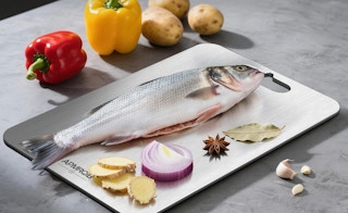a fish and seasonings on a cutting board next to peppers and potatoes
