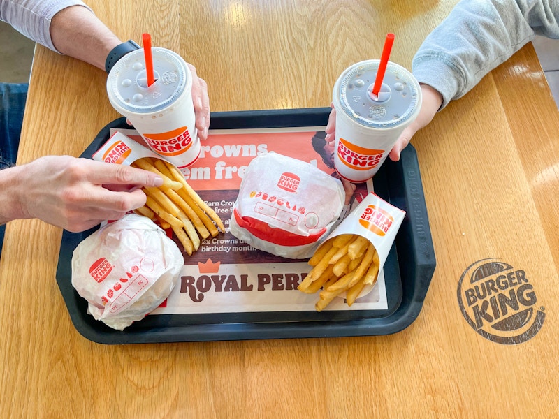 a tray with 2 burgers, 2 fries, and 2 drinks being grabbed by two people