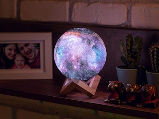 A Galaxy Moon Lamp lit up on its stand on someone's mantel