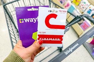 person holding wayfair and cinemark gift cards over a walgreens cart
