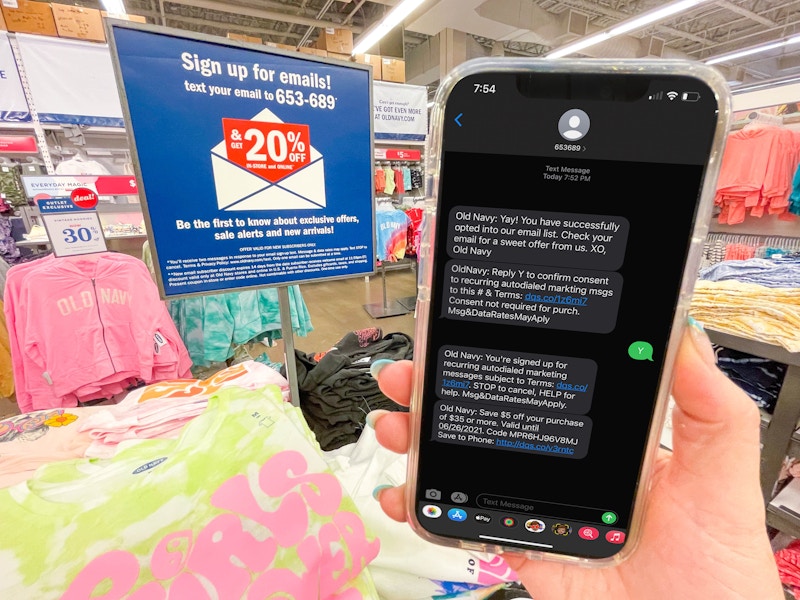 hand holding cellphone with text from old navy in front of sign for text for email