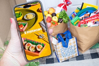 someone with Instacart on their phone in front of some bags on the porch