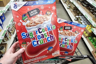 person holding a box of sugar cookie toast crunch cereal with another box in a cart