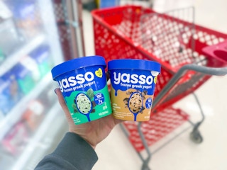 hand holding 2 yasso frozen greek yogurt in front of target cart