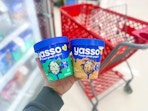 hand holding 2 yasso frozen greek yogurt in front of target cart