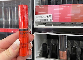 A hand holding NYX butter gloss in a store.