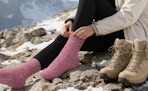 a person putting on pink wools socks on a mountain
