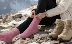 a person putting on pink wools socks on a mountain