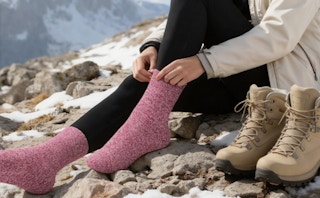 a person putting on pink wools socks on a mountain