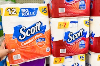 hand holding pack of toilet paper next to stacked paper towels