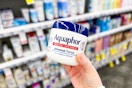 person holding a tub of aquaphor in front of shelves
