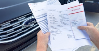 Someone comparing the declaration pages from different auto insurance policies in front of a car