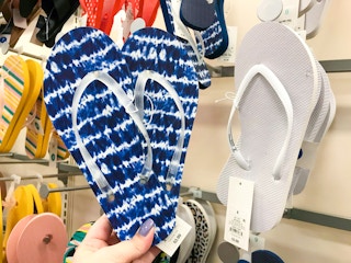 hand holding pair of flip flops in front of other flip flops