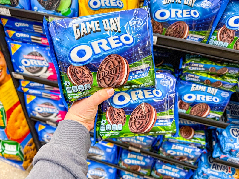 person holding 2 packages of game day oreos in front of an oreo display