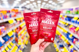 person holding 2 bags of halls cough drops in an aisle