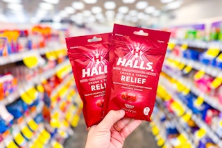 person holding 2 bags of halls cough drops in an aisle