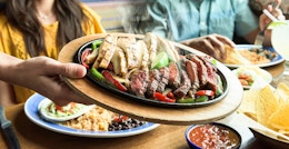 on the border server placing plate of fajitas on table in restaurant