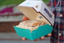 Someone holding a Cinnabon cinnamon roll in a box