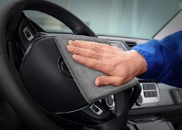 a person using a grey cloth to clean a steering wheel