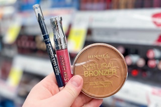 hand holding rimmel eyeliner, lip gloss, and bronzer