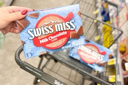 person placing swiss miss hot chocolate mix in a cart