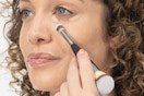 a woman putting on concealer with an it cosmetics brush