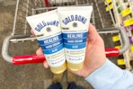 person holding 2 bottles of gold bond hand cream over a cart