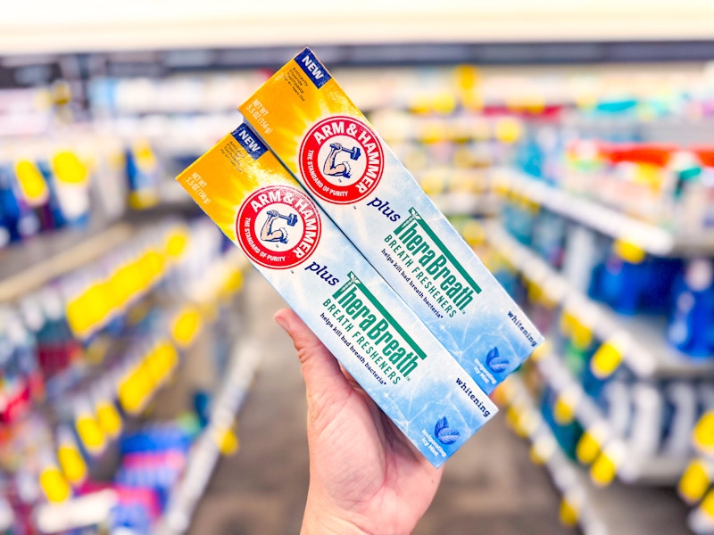 person holding 2 tubes of arm and hammer toothpaste in an aisle