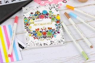 Metallic markers and a coloring book on a white wooden table