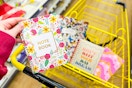 hand holding a floral notebook above a shopping cart