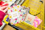 hand holding a floral notebook above a shopping cart