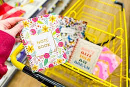 hand holding a floral notebook above a shopping cart