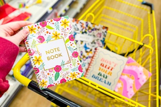 hand holding a floral notebook above a shopping cart