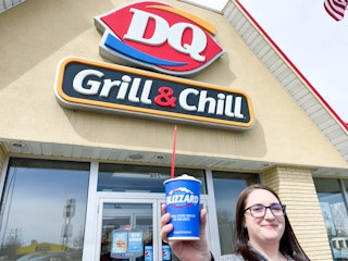 a person standing in front of the dairy queen sign holding up a blizzard