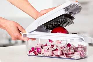A person using a Fullstar vegetable chopper to chop a red onion.