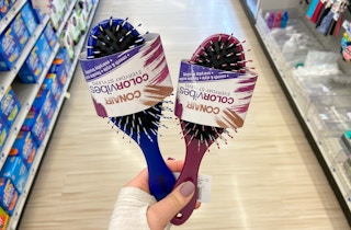 A person's hand holding two Conair hairbrushes in an aisle at Rite Aid.