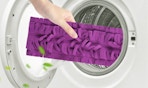 a hand putting a purple mop pad in a washing machine